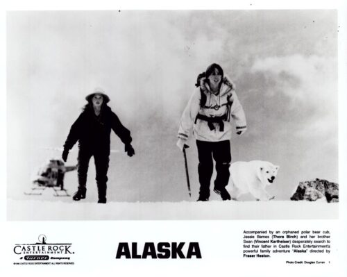 Two people trek through snow with a white dog in front of a misty mountainscape; promotional shot for the film Alaska by Castle Rock.