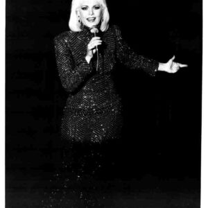 Female singer on stage, microphone in hand, wearing a glittering sequin blazer, performing.