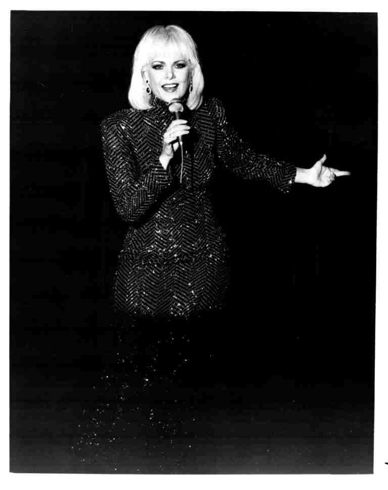 Female singer on stage, microphone in hand, wearing a glittering sequin blazer, performing.