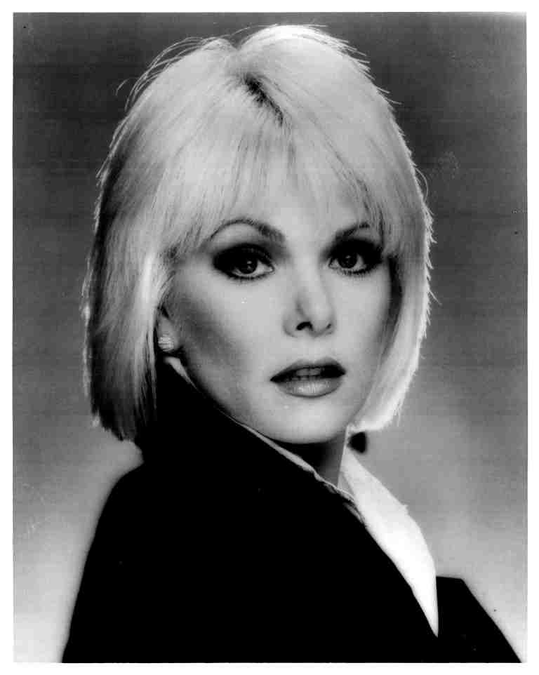 Black-and-white studio portrait of a woman with short blonde hair, looking at the camera.