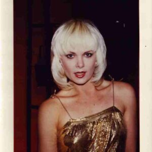 Portrait of a woman with platinum blonde hair in a gold sequined dress, looking at the camera.