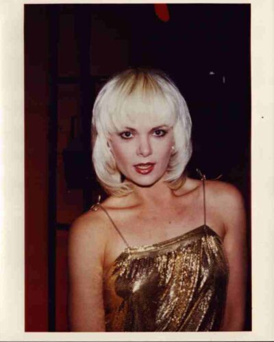 Portrait of a woman with platinum blonde hair in a gold sequined dress, looking at the camera.