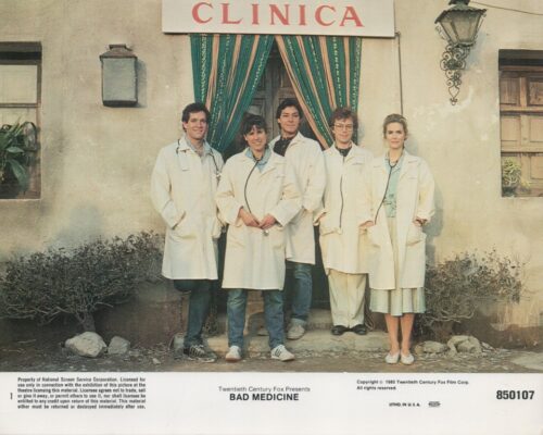 Group of five people in white lab coats standing outside a clinic with green curtains and a red 'CLINICA' sign, a film poster for Bad Medicine.
