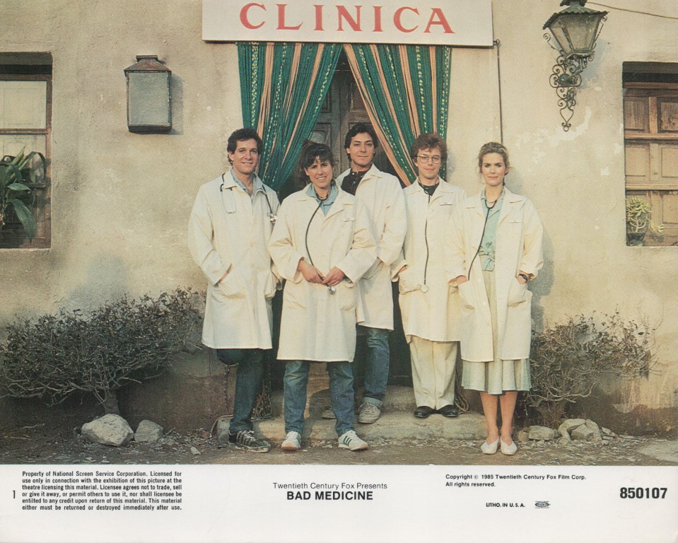 Group of five people in white lab coats standing outside a clinic with green curtains and a red 'CLINICA' sign, a film poster for Bad Medicine.