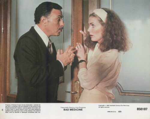 A man in a dark suit and a woman in a pale pink dress argue anxiously at a doorway, pressed close to the frame.