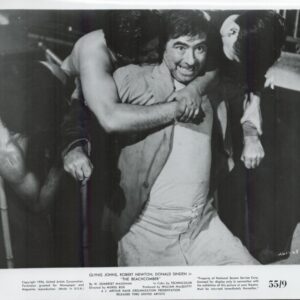 Black-and-white still of a man being restrained by two others in a scuffle, smiling as he is held back from a fight (film still from The Beachcomber).