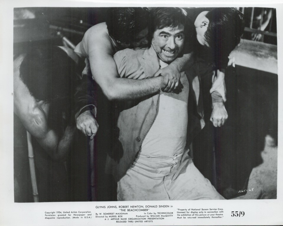 Black-and-white still of a man being restrained by two others in a scuffle, smiling as he is held back from a fight (film still from The Beachcomber).