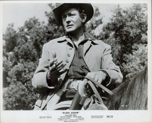 Black-and-white still of a cowboy on a horse, wearing a hat and jacket, gesturing with his left hand.