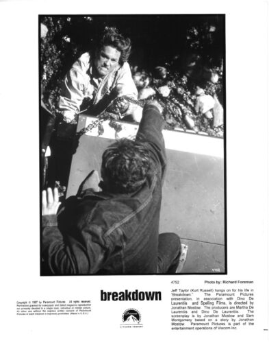 Black-and-white still from Breakdown: a man outside the car leans over and reaches toward another man inside the vehicle in a tense scene.