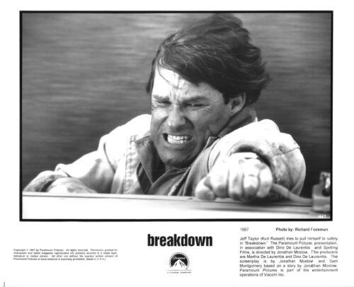 Close-up of a man grimacing and reaching out from a car window on a black‑and‑white poster for the film Breakdown.