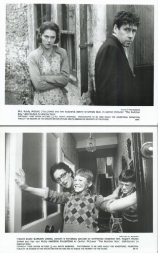 Black-and-white film still: a woman with crossed arms and a man in a dark coat stand outside a weathered building, tense.