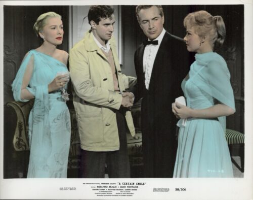Four adults in a formal living room: a man in a beige trench coat shakes hands with a man in a tuxedo while two women in teal gowns look on.