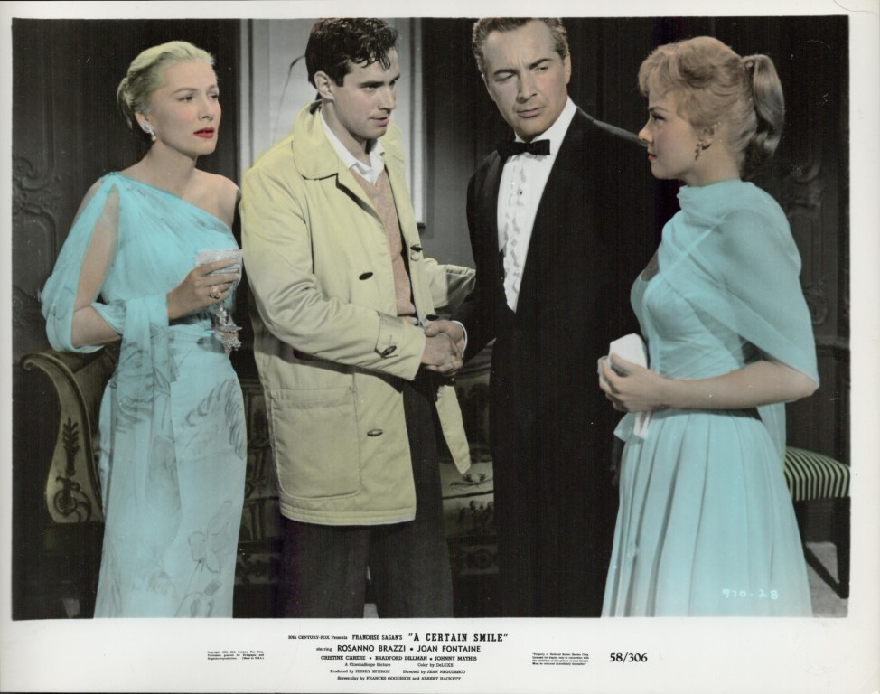 Four adults in a formal living room: a man in a beige trench coat shakes hands with a man in a tuxedo while two women in teal gowns look on.
