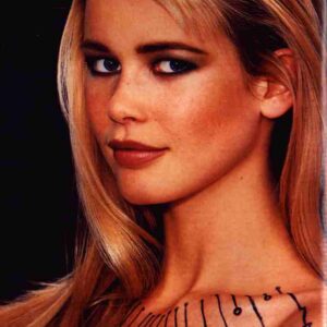 Close-up portrait of a blonde woman with decorative black line markings along her neckline, looking over her shoulder to the right.