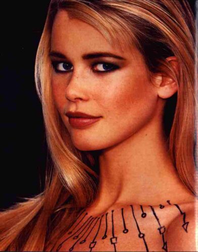 Close-up portrait of a blonde woman with decorative black line markings along her neckline, looking over her shoulder to the right.