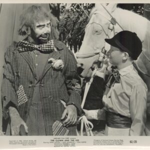 Clown in a torn suit chats with a boy in a cap; a white horse stands nearby.