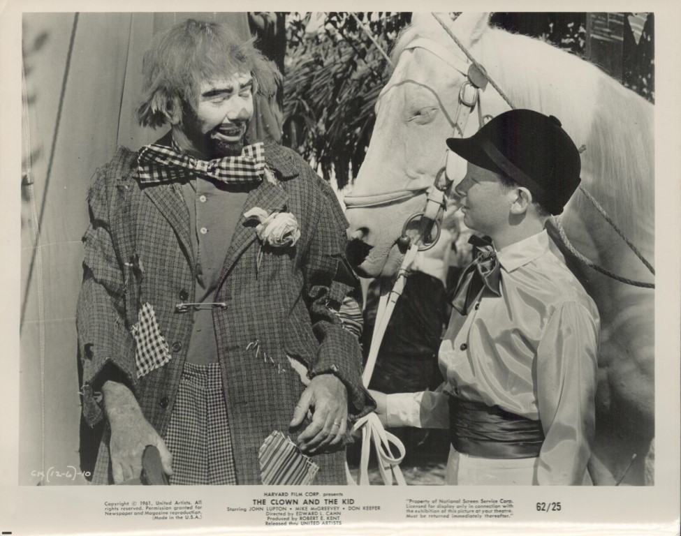 Clown in a torn suit chats with a boy in a cap; a white horse stands nearby.