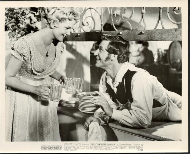 Vintage scene: woman in dress serves drinks to a man at a bar counter, smiling.