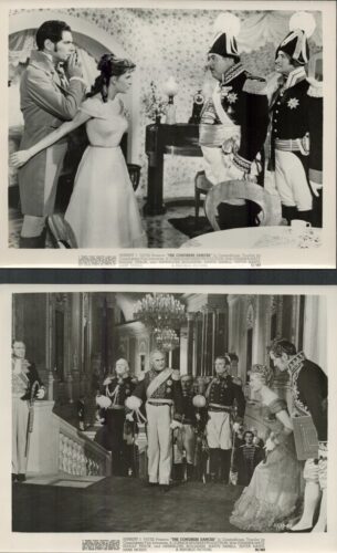 Man and woman in period dress are restrained by two plumed soldiers in ceremonial uniforms in a formal dining room setting.