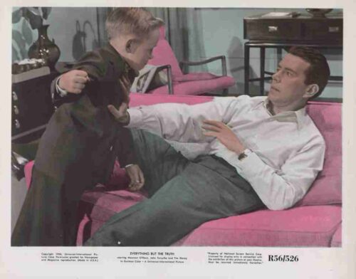 Man lounging on a bright pink sofa as a young boy in a suit reaches toward him, in a retro living room.