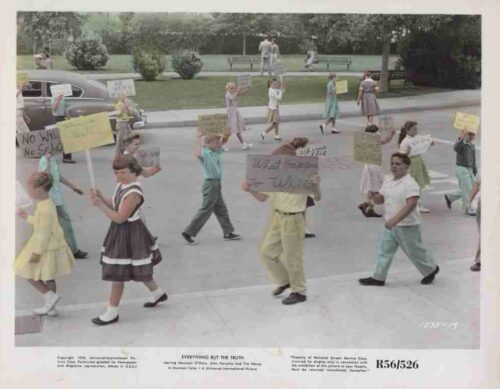 Group of children marching in a street protest, each carrying handmade signs with slogans.