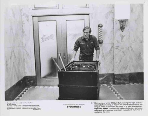 Man in a work shirt pushes a large cleaning cart through a marble-floored lobby with double doors behind him.