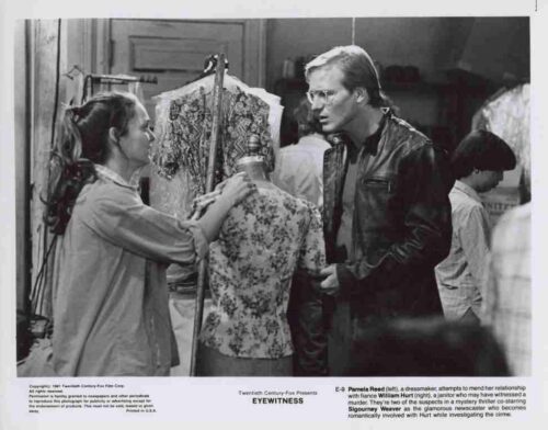 Two people in a costuming studio adjust a floral-patterned dress form while a man observes nearby, mid-design fitting scene.