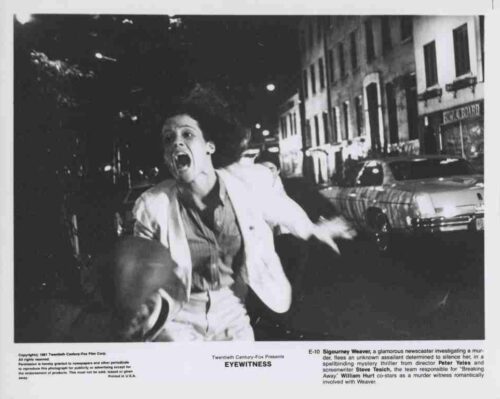 Black-and-white street scene with a woman in a light suit running toward the camera, mouth open in a scream, holding a hat as cars line the curb at night.