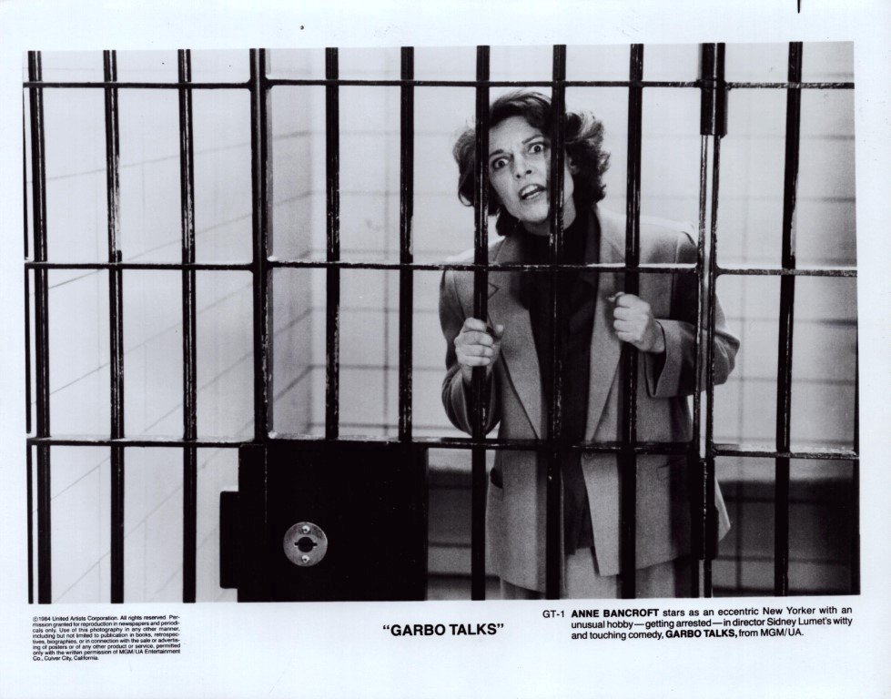 Still from Garbo Talks showing a distressed woman behind jail bars, gripping the bars with a wide-eyed expression.