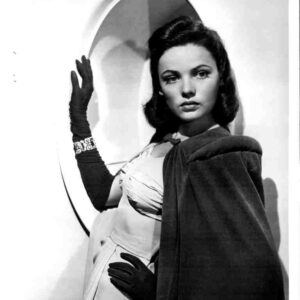 Black-and-white portrait of a glamorous woman in a formal gown and long gloves, posing with a curved backdrop behind her.