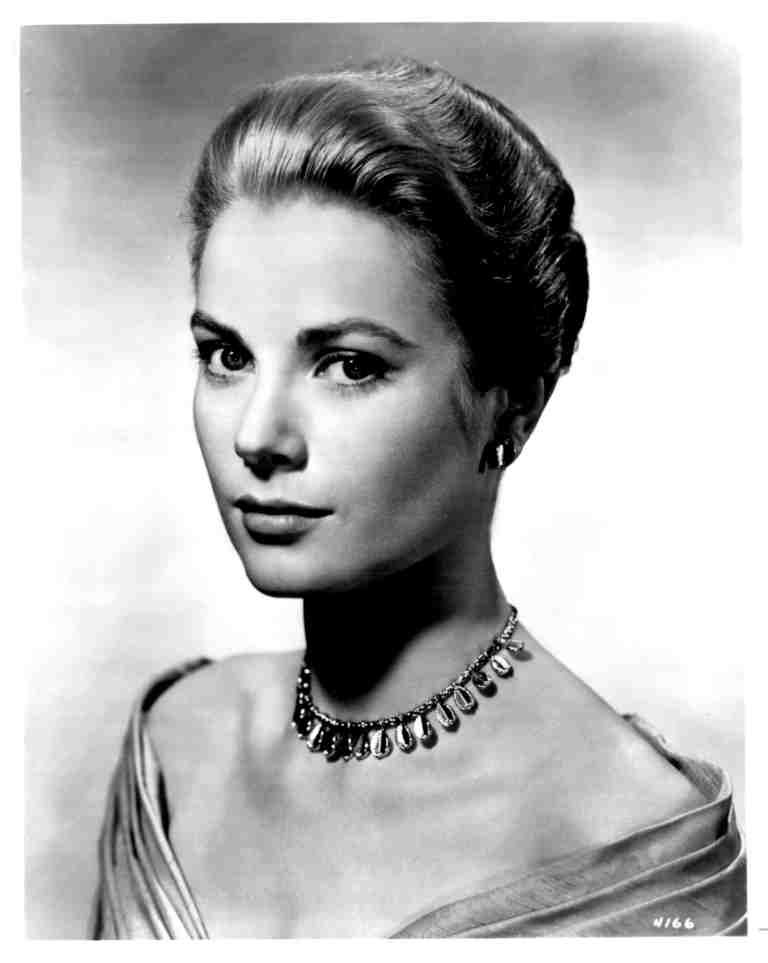 Black-and-white portrait of a young woman with an elegant updo hairstyle, wearing a teardrop necklace and off-shoulder gown.