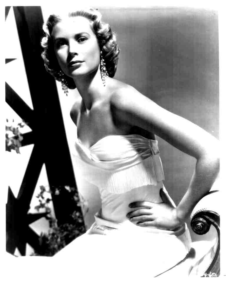 Vintage black-and-white portrait of a glamorous woman in a strapless gown and chandelier earrings, posed with one hand on her hip.