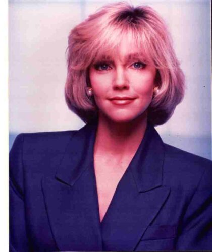 Professional head-and-shoulders portrait of a woman with pink hair wearing a dark blazer, facing the camera.