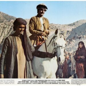 Two men in traditional Middle Eastern clothing walk a white horse through a desert crowd, mountains in the background; appears to be a vintage film poster with credits at the bottom.