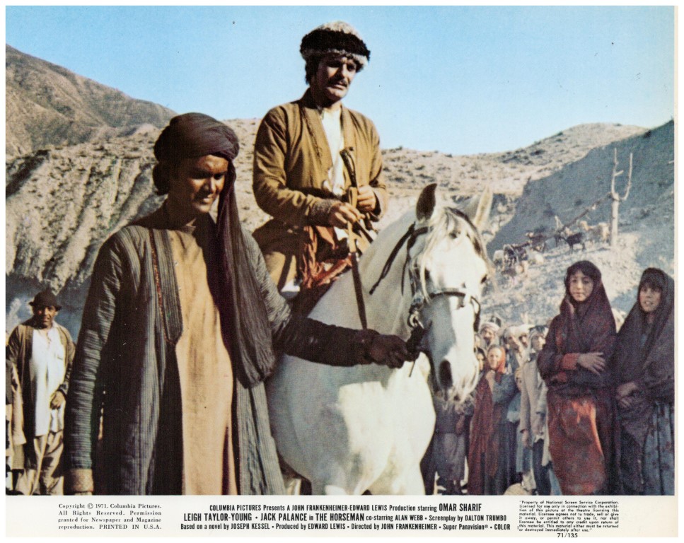 Two men in traditional Middle Eastern clothing walk a white horse through a desert crowd, mountains in the background; appears to be a vintage film poster with credits at the bottom.