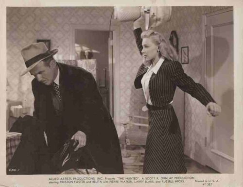 Man in a fedora and dark overcoat bends over a table as a woman in a pinstripe dress raises her arm in a tense 1940s film-set moment.