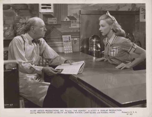Still from a 1960s film: an older man with suspenders reads a magazine at a diner counter while a nurse in a checkered uniform talks to him.
