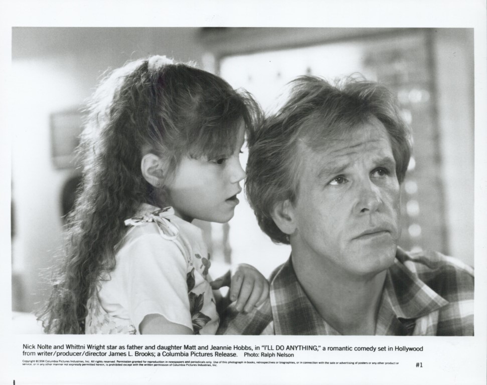 Black-and-white film still of a man and a young girl closely watching something off-camera, conveying a thoughtful moment between father and daughter in a family scene from I'll Do Anything.
