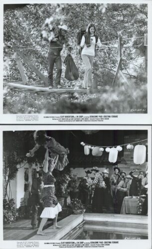 Two young people cross a rope bridge through a forest, one carrying a large bag between them.