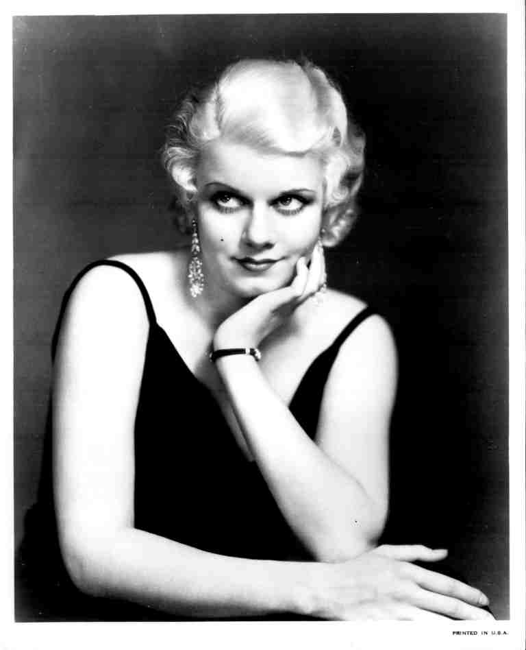Black-and-white portrait of a glamorous woman in a black evening dress, resting her chin on her hand.