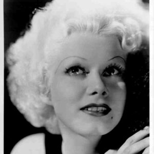 Black-and-white portrait of a woman with platinum curls, bold eyebrows, and red lipstick looking upward slightly to the side.