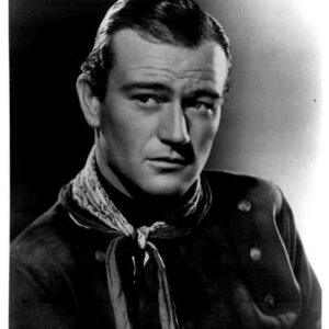 Black-and-white studio portrait of a man in a western-style outfit with a neck scarf, gazing slightly to the side.