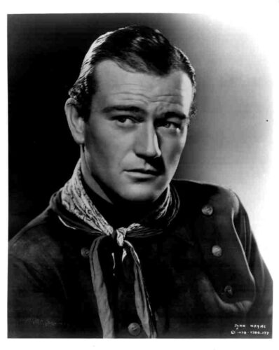 Black-and-white studio portrait of a man in a western-style outfit with a neck scarf, gazing slightly to the side.