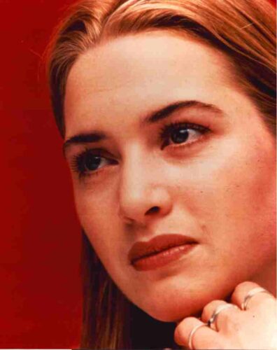 Close-up portrait of a woman with light skin and light brown hair against a solid red background, looking to the side.