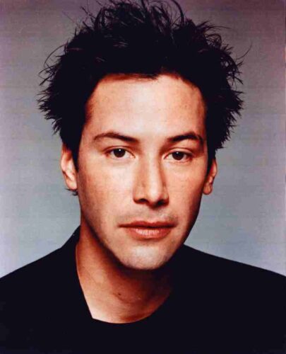 Head-and-shoulders portrait of a man with spiky dark hair, wearing a black shirt, against a neutral gray background.