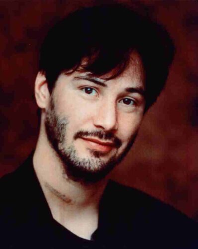 Portrait of a man with dark hair and light stubble, wearing black, looking at the camera against a brown background.
