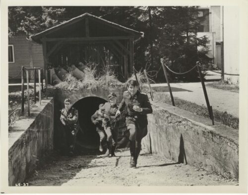 Uniformed soldiers sprinting from a tunnel entrance into a courtyard, toward the camera.