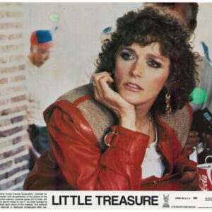 Woman with curly hair in a red leather jacket rests her chin on her hand at a film poster for 'Little Treasure', with a Coca-Cola can on the table in front.