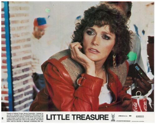 Woman with curly hair in a red leather jacket rests her chin on her hand at a film poster for 'Little Treasure', with a Coca-Cola can on the table in front.
