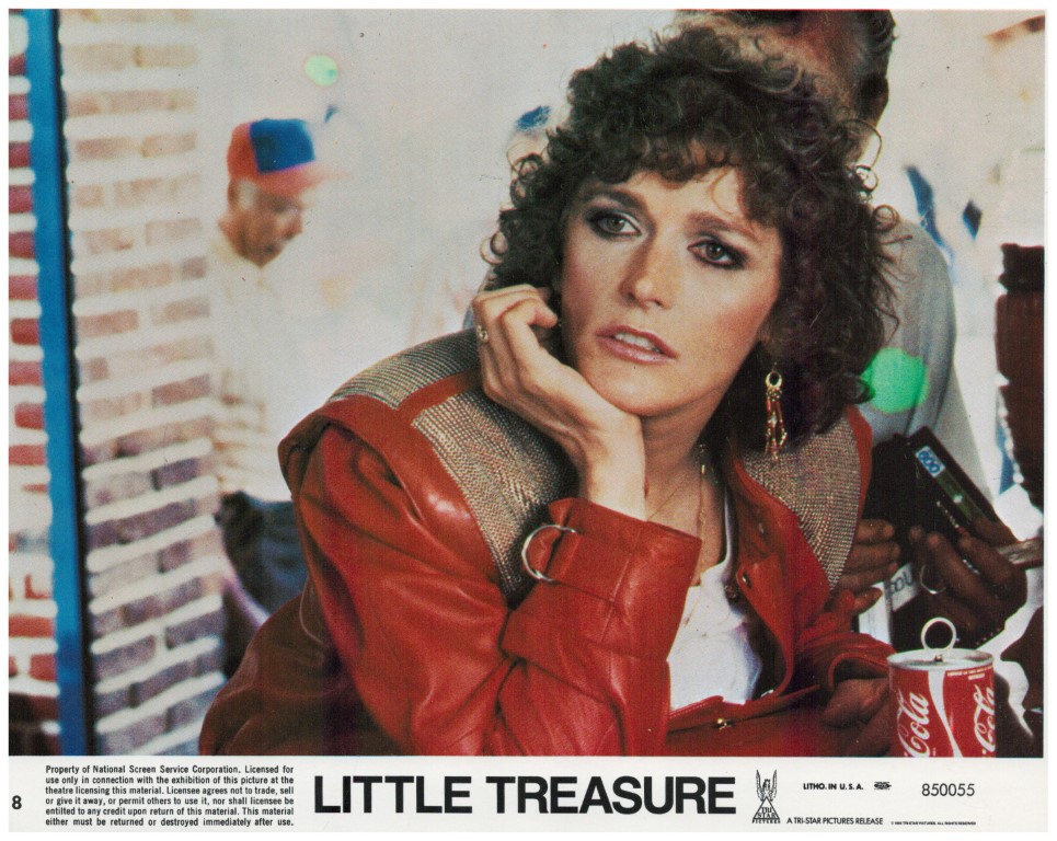 Woman with curly hair in a red leather jacket rests her chin on her hand at a film poster for 'Little Treasure', with a Coca-Cola can on the table in front.